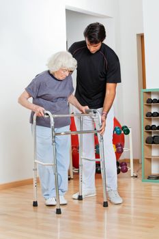 Full length of a trainer assisting senior woman in moving walker