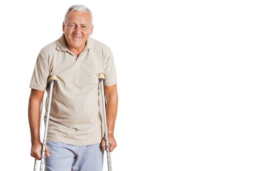 Portrait of smiling senior man on crutches standing over white background.