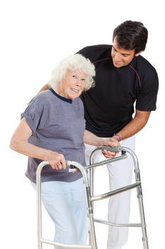 Portrait of a happy senior woman holding walker while trainer assisting her over white background