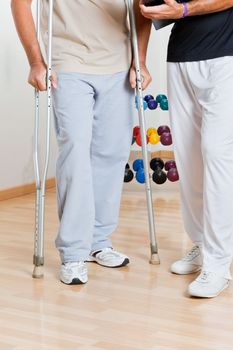 Low section of a man holding crutches standing by trainer