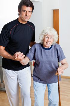 Portrait of a happy trainer assisting woman with walking stick