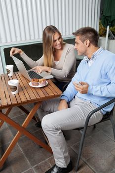 Young woman pointing at laptop screen to man while sitting at cafe