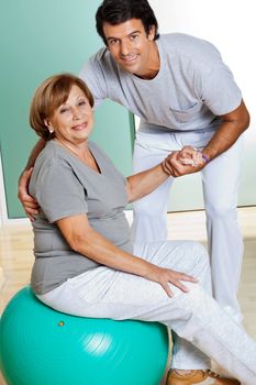 Portrait of male therapist helping senior woman sitting on fitness ball
