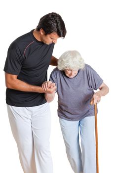 Young trainer assisting senior woman holding walking stick over white background