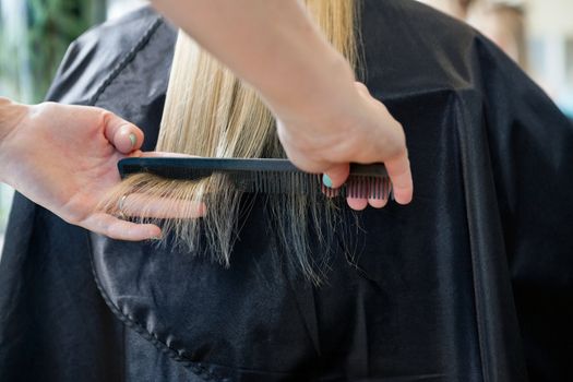 Hairstylist combing hair of a blonde female customer before haircut at salon