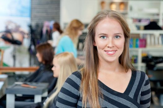 Portrait of young female hairdresser smiling with people in background