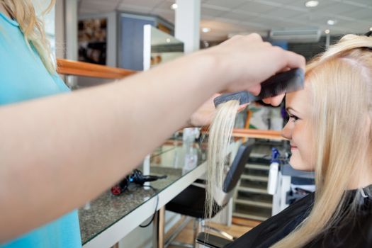 Cropped image of hairstylist combing hair of young female customer before haircut at salon