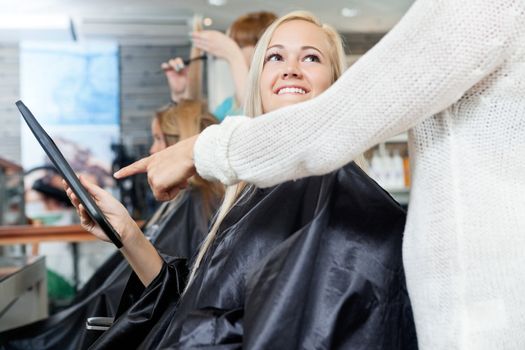 Woman looking at hairdresser while she points on digital tablet's screen