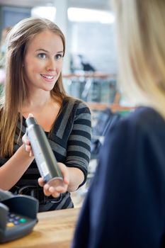 Young female hairstylist showing hair product to customer at counter