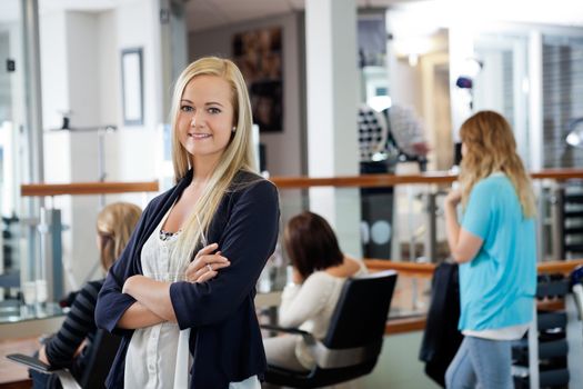 Portrait of beautiful female owner of parlor standing arms crossed with customers in background