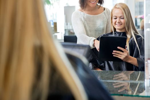 Mirror reflection of female customer holding digital tablet with hairdresser standing behind her