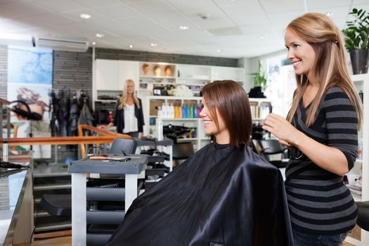 Young female hairdresser standing behind customer's chair after giving a haircut