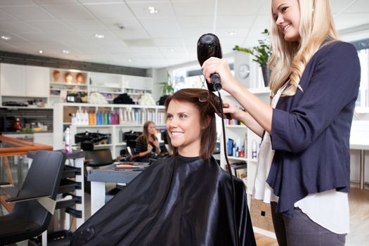 Hairdresser drying female customer's hair in beauty salon