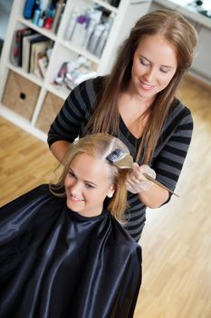 High angle view of beautician applying hair dye on female customer's hair - shallow DOF focus on hair stylist