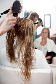 Hairdressers hands drying long blond hair with blow dryer at parlor