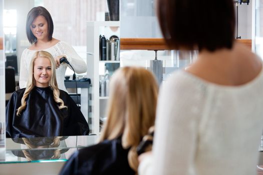 Mirror reflection of young woman getting her curled by stylist at parlor
