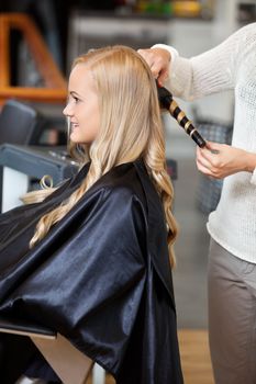 Side view of a young woman getting her hair curled by beautician at parlor