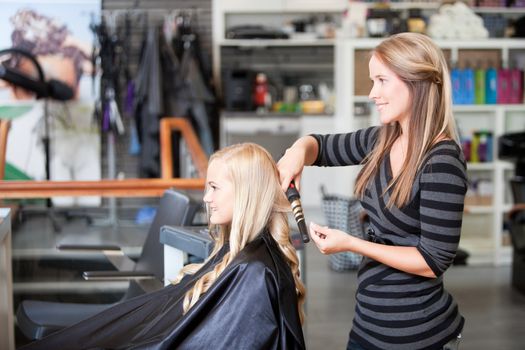 Stylist curling womans hair in beauty salon .