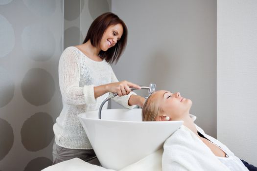 Beautician smiling while washing hair of female customer at beauty salon