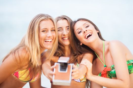 three teenager beautiful girls taking selfie with old camera on the beach