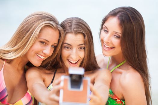 three teenager beautiful girls taking selfie with old camera on the beach