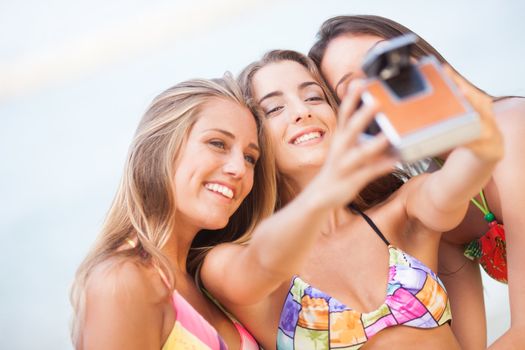 three teenager beautiful girls taking selfie with old camera on the beach