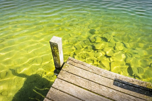 Part of a jetty over a lake of weathered wood with green-blue water and small waves.