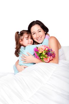 Cute child giving flowers and hug to mom in bed, mother day or hospital concept, isolated.