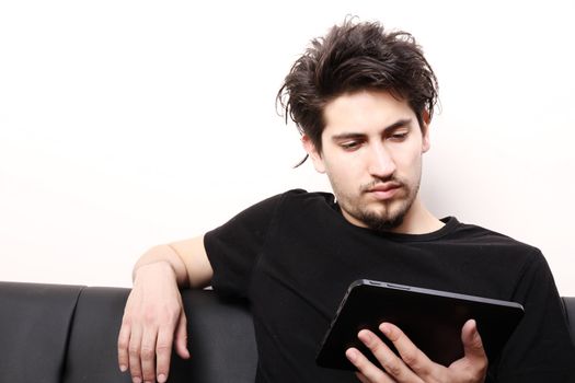 A young hispanic man sitting on the sofa holding a Tablet PC.