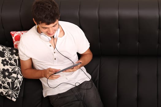 A young, latin man with a Tablet PC and Headphones on the Sofa
