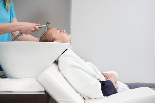 A young blond caucasian woman having her hair washed and rinsed at a beauty salon.