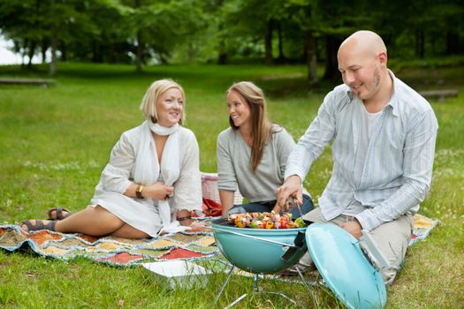 Male cooking food on bbq with friends in park