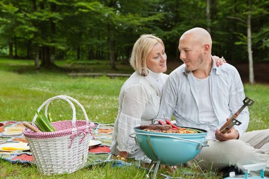Mature couple in casual clothes looking at each other while on an outdoor picnic in forest park