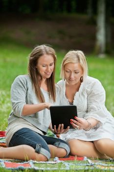 Caucasian mother and daughter using digital tablet while sitting comfortably on a picnic blanket