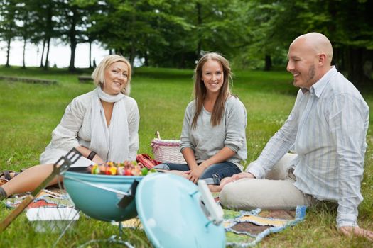 Happy Caucasian friends on picnic with portable barbeque in forest park