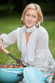 Portrait of an attractive woman in casual wear cooking food on portable barbecue