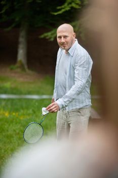 Portrait of mature man in casual wear with racquet and birdie ready to serve