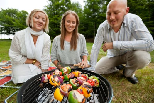 Three friends cooking shish kebabs over portable barbecue