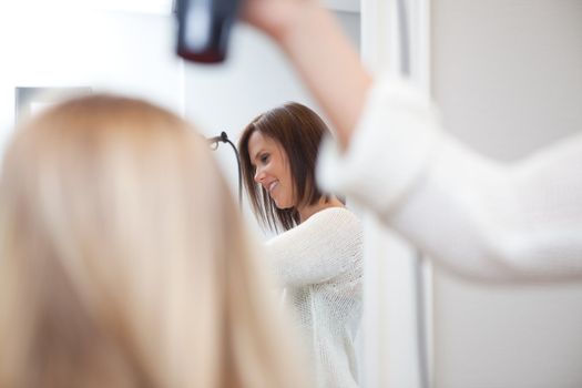 Stylist drying womans hair in beauty salon .