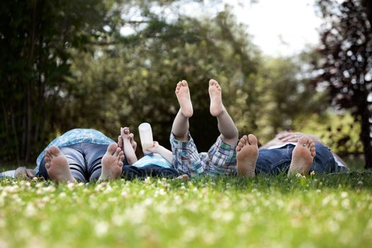 Young family with two kids and pregnant mother laying down in park with feet towards camera
