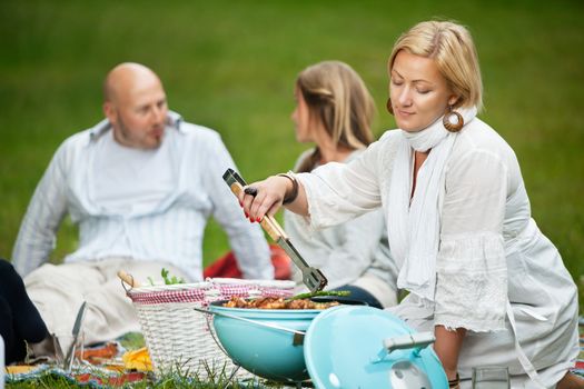 Woman cooking food on a portable barbecue while man and girl sit in background