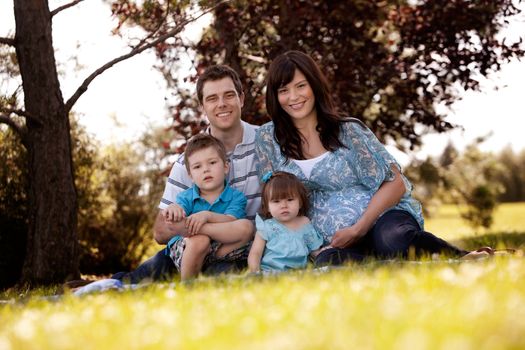 Portrait of young family in park with pregnant mother