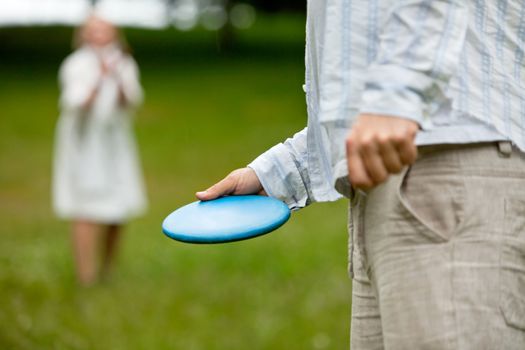 Midsection of man in casual clothing ready to throw Frisbee with woman in background