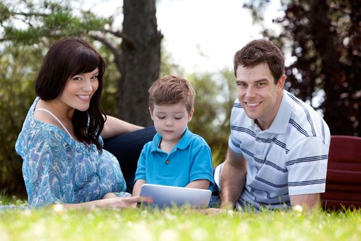 Young boy looking a digital tablet with parents in park