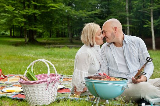 Romantic couple on picnic with food on portable barbecue in forest park
