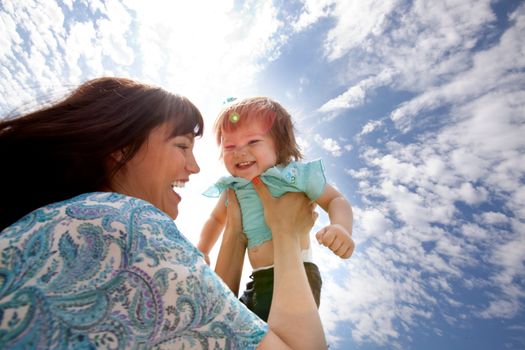 Happy smiling mother holding young toddler daughter in air against sky