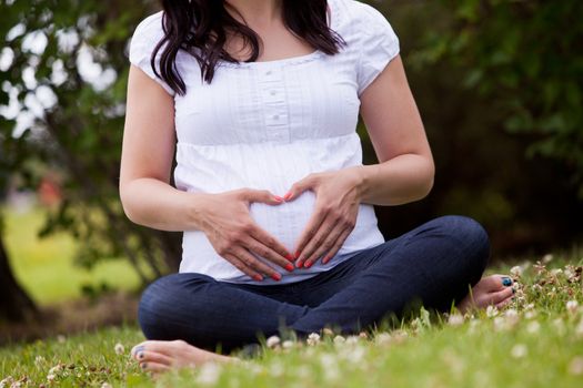 Faceless pregnant woman in third trimester sitting in park