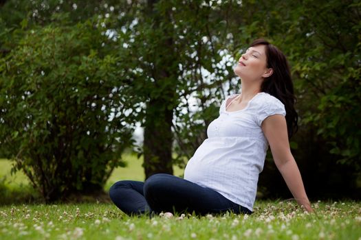 Relaxed calm pregnant woman in third trimester in park with eyes closed