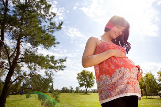 Attractive pregnant woman outdoors in park - shot towards sun with lens flare