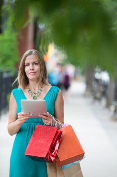 Portrait of a pretty young woman with shopping bags and digital tablet on sidewalk